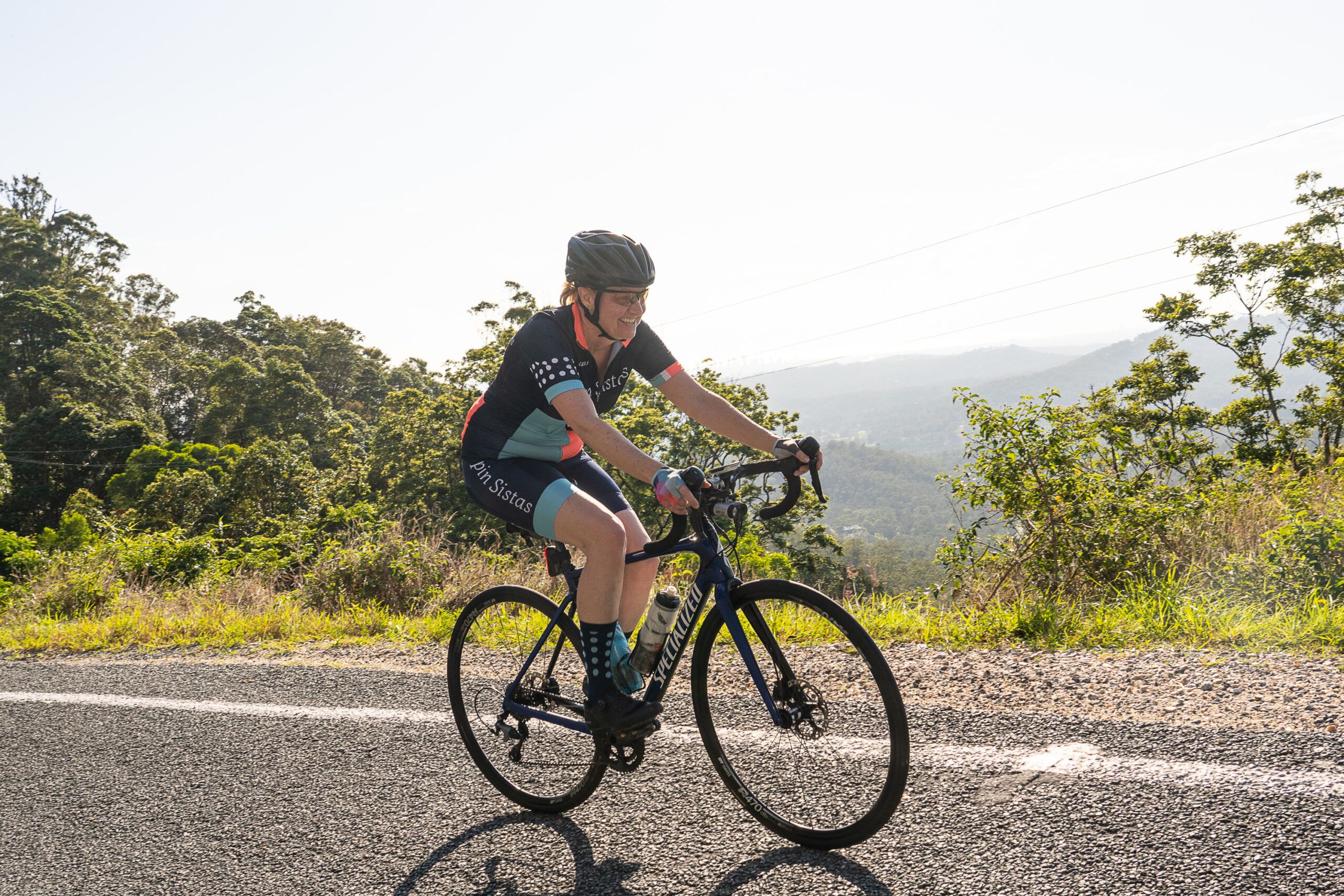 A Spin Sistas cyclist climbing a quiet hinterland road